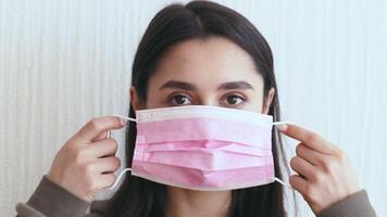 A young Caucasian woman puts on a pink mask while sitting at home. She appears unwell, indicating symptoms of flu or cold during a time of isolation due to illness. video