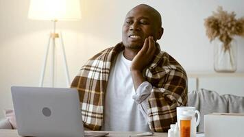 A man in his 30s focused on his laptop while wrapped in a blanket. The living area features warm lighting and personal items, creating a relaxed atmosphere for productivity. video