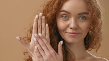 A woman with curly red hair is gently applying hand cream to her hands in a calm, minimalist environment. The soft lighting complements her natural beauty. video