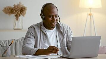 A man in his 30s with a headset actively engages in a virtual meeting at home. He sits at a desk with a laptop, conveying enthusiasm, and is surrounded by a cozy setting. video