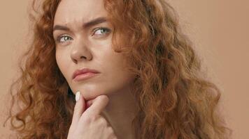 A young woman with striking curly hair is deep in thought, resting her chin on her hand. She gazes upwards, reflecting with a serious expression against a subtle background. video