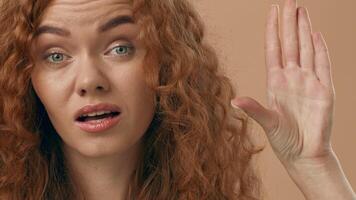 A woman with long, curly hair stands in a softly lit room, making a gesture with her hand to indicate a small size. She appears focused and engaged, conveying a clear message. video