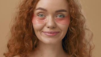 A young woman with curly hair uses under-eye patches, focused on skincare. She gently applies the patches while maintaining a serene expression, highlighting a self-care moment. video