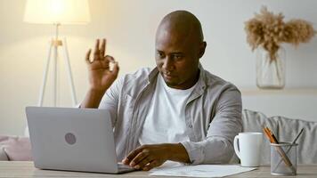 A man sits at a wooden desk in a modern home office, engaging with his laptop. He appears focused, with soft lighting enhancing the calm atmosphere around him. video