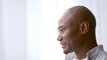 African American man in his 30s sits comfortably at home, sipping coffee and looking thoughtful. The bright light from the window creates a peaceful atmosphere for relaxation, copy space video