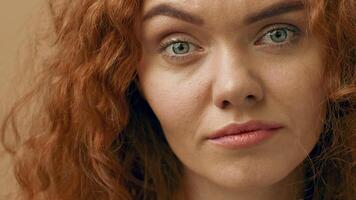 A woman with curly red hair and green eyes gazes directly at the viewer, showcasing her natural beauty in a well-lit indoor setting. Her expression is calm and inviting. video