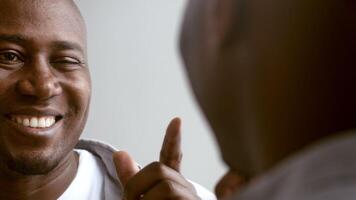 African American man in his 30s smiles warmly while looking into a mirror at home. The room is softly lit, creating a cozy and relaxed atmosphere. His expression conveys joy and contentment. video