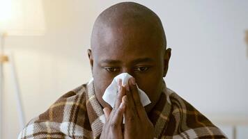 A man in his 30s sits quietly, wrapped in a warm blanket, holding a tissue to his face. He looks contemplative and emotional, surrounded by a softly lit home environment. video