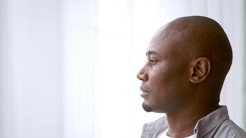A man in his 30s stands thoughtfully in a bright, contemporary home, gazing into the distance. Natural light streams through the windows, creating a calm atmosphere, copy space video
