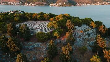 Aerial view of island covered with forest trees and circular labyrinth on top at sunset. Sea landscape with coastal town. Lavender labyrinth in Rogoznica, Croatia video