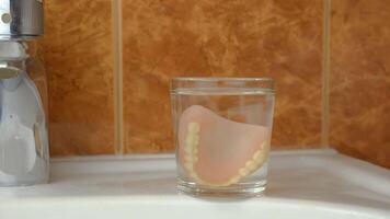 On the sink there is a glass in which a woman's hand puts a false jaw for cleansing video