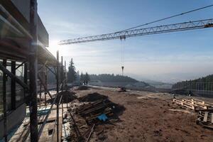 The exterior of a business building under construction is surrounded by trucks, cranes, and various construction materials, creating a bustling scene of an expansive industrial worksite in progress photo