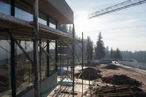 The exterior of a business building under construction is surrounded by trucks, cranes, and various construction materials, creating a bustling scene of an expansive industrial worksite in progress photo