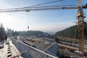 The exterior of a business building under construction is surrounded by trucks, cranes, and various construction materials, creating a bustling scene of an expansive industrial worksite in progress photo
