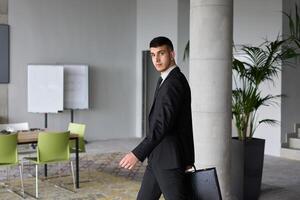 A determined businessman in a black suit confidently walks through the office, embodying professionalism and focus as he heads towards new challenges photo
