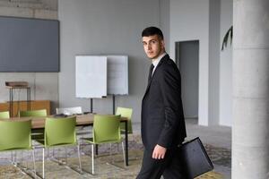 A determined businessman in a black suit confidently walks through the office, embodying professionalism and focus as he heads towards new challenges photo