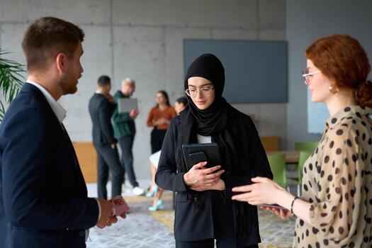 A diverse group of business professionals engages in a conversation during a work break in the office, with their colleagues visible in the background, fostering collaboration and connection photo