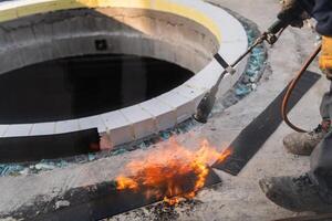 An industrial worker uses fire to soften a rubber underlay for floor insulation, showcasing precision and skill in a critical step of the construction process photo