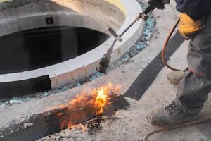 An industrial worker uses fire to soften a rubber underlay for floor insulation, showcasing precision and skill in a critical step of the construction process photo