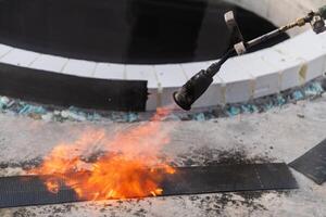 An industrial worker uses fire to soften a rubber underlay for floor insulation, showcasing precision and skill in a critical step of the construction process photo