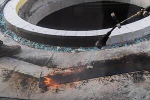 An industrial worker uses fire to soften a rubber underlay for floor insulation, showcasing precision and skill in a critical step of the construction process photo