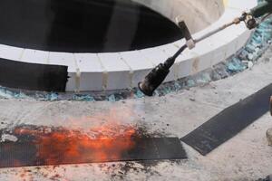 An industrial worker uses fire to soften a rubber underlay for floor insulation, showcasing precision and skill in a critical step of the construction process photo