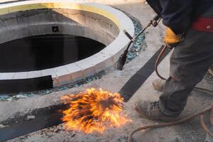 An industrial worker uses fire to soften a rubber underlay for floor insulation, showcasing precision and skill in a critical step of the construction process photo