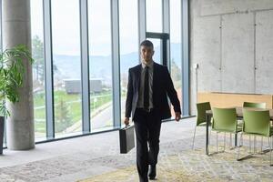 A determined businessman in a black suit confidently walks through the office, embodying professionalism and focus as he heads towards new challenges photo