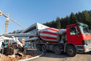 The exterior of a business building under construction is surrounded by trucks, cranes, and various construction materials, creating a bustling scene of an expansive industrial worksite in progress photo