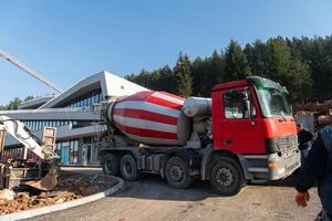 The exterior of a business building under construction is surrounded by trucks, cranes, and various construction materials, creating a bustling scene of an expansive industrial worksite in progress photo