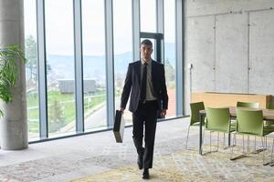 A determined businessman in a black suit confidently walks through the office, embodying professionalism and focus as he heads towards new challenges photo