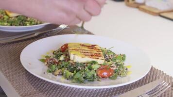 Woman adding sauce to salad with grilled tofu on dining table video