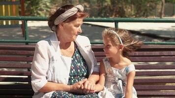 Grandmother and granddaughter holding hands while talking on park bench video