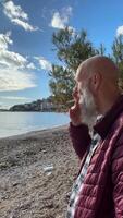Close-up of a man with a gray beard smoking a cigarette against the background of the sea. bad habits. Thoughtful man smoking a cigarette with a filter. High-quality 4k footage video