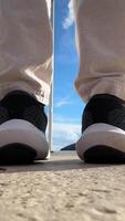 The legs of a man walking along the pier to the flagpole towards the sea. embankment on a sunny day with the mountains in the background. The concept of recreation and travel. High-quality 4k footage video