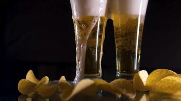 Super slow motion a glass of cold beer on a table in a black background, Potato chips are falling on a wooden table, Golden beer natural foam, natural alcoholic cold drink. video