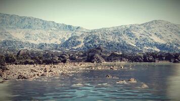 Rocky shoreline with clear water and mountain backdrop at midday video