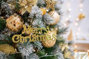 A close-up of a merry christmas text toy on a Christmas tree with lights on background. High quality photo
