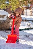 Child playing with with a child's shovel and snow in the backyard of the house in winter, Christmas time. High quality photo