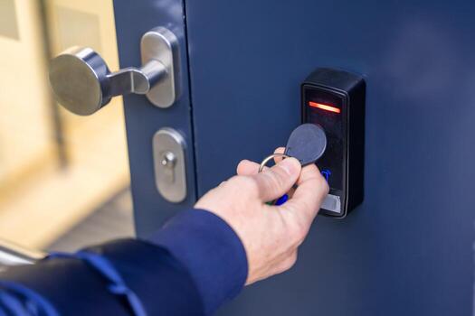 Close up view of person using a electric lock key fob to access a building via a reader of entry system mounted on a house wall. High quality photo