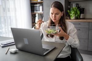 Tired woman eats food ordered at delivery service while sitting in her home office in front of laptop during lunch break. High quality photo