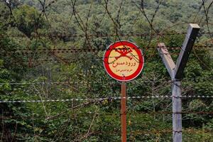 Gilan Province, Iran - September 28, 2024 - Barbed wire and warning signs delineate the border territories of Iran and Azerbaijan, surrounded by greenery and vegetation. photo