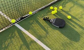 Padel racket and padel ball on a green court in the sunset photo