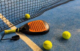 padel racket and yellow balls placed on court near net photo