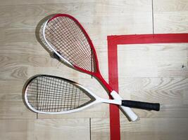 Two rackets and two squash balls lie on the parquet floor. Horizontal photo
