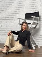 middle aged business woman in smart casual attire and standing near chair on grey photo