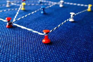 Network visualization with colored pins and string on blue fabric, connection concept photo