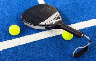 Black professional paddle tennis racket and ball on blue background. Horizontal sport theme poster, greeting cards, headers, website and app photo