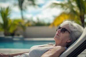 Old woman relaxes on sun lounger by swimming pool photo