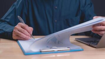 Professional examines and signs important documents while utilizing laptop focus is on meticulous attention to detail in paperwork management and efficient workflow photo